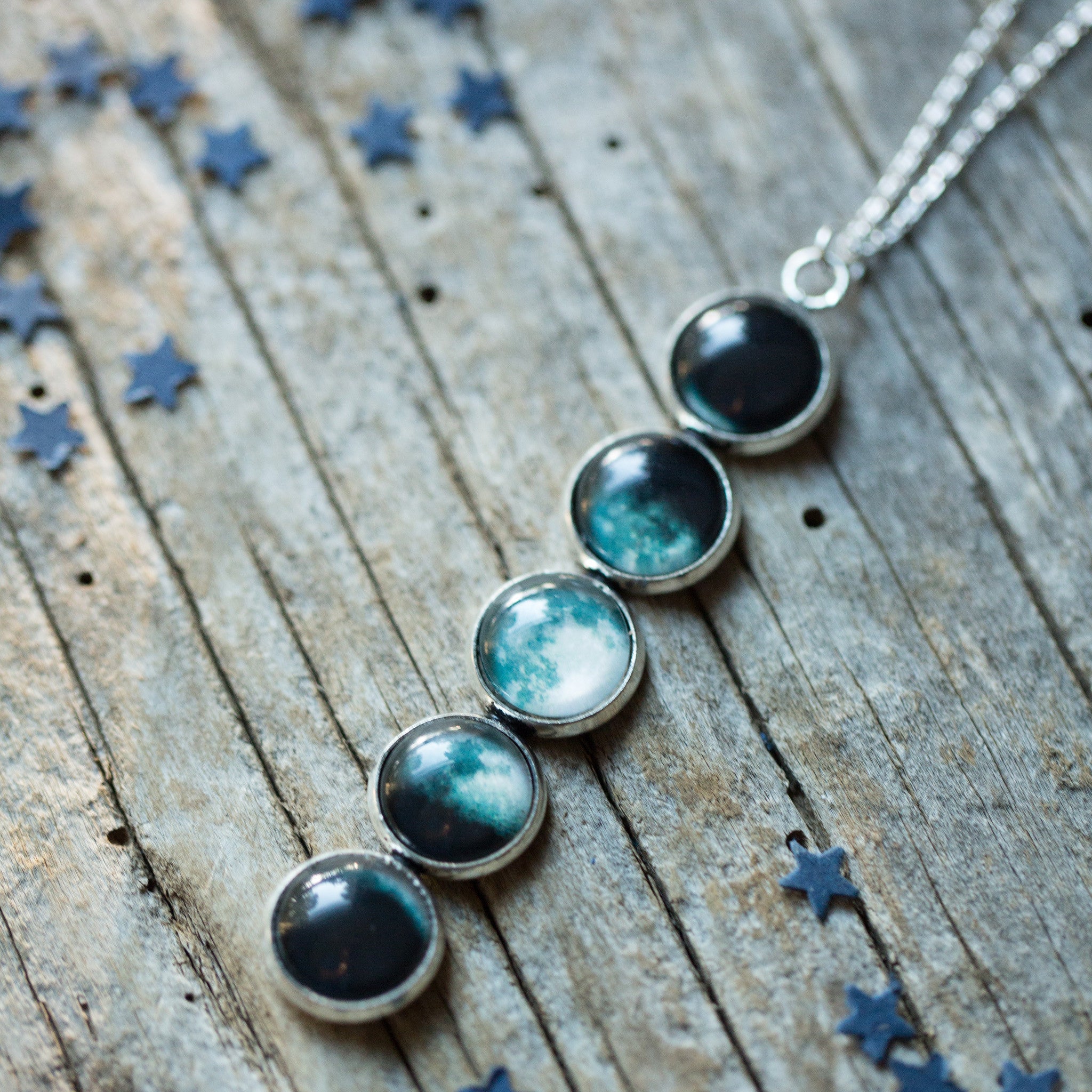 Introducing the Moon Phase Pendant Necklace: a breathtaking piece adorned with five round pendants, each beautifully depicting the phases of the moon against a starry background, capturing the splendor of the lunar cycle.