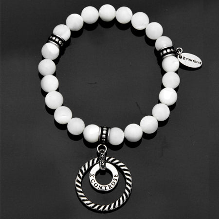 The Heiress Bracelet features white beads and silver accents, with a circular pendant inscribed with "X CONTROSE" on a dark background. Its stainless steel components enhance its elegance, making the bracelet a timeless accessory.