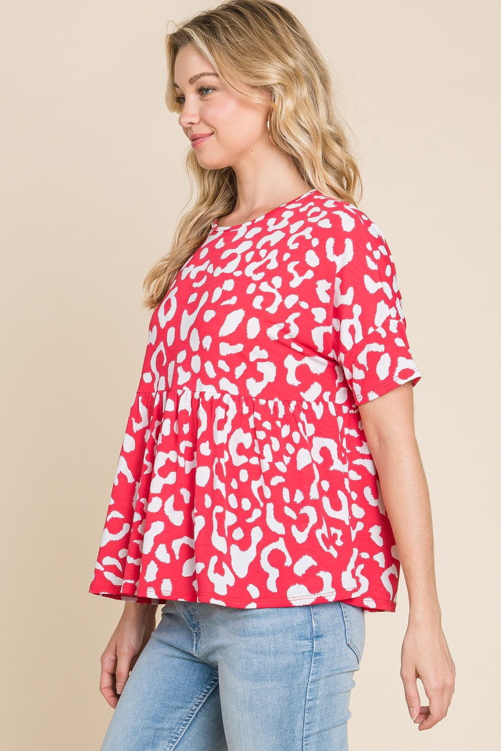 A person in a red and white BOMBOM Leopard Peplum Babydoll Blouse and blue jeans stands against a beige background.