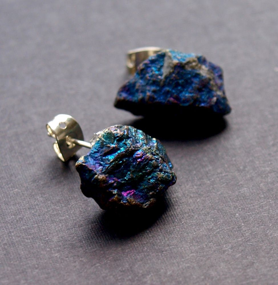 A pair of Raw Peacock Ore Chunk Earrings glisten on a dark surface, making a bold statement in unique jewelry design.