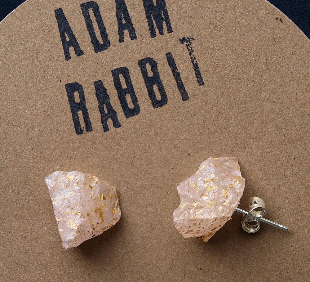 A pair of Gold Splatter & Raw Rose Quartz Chunk Earrings, featuring unpolished stones on silver posts, elegantly displayed on a dark surface.