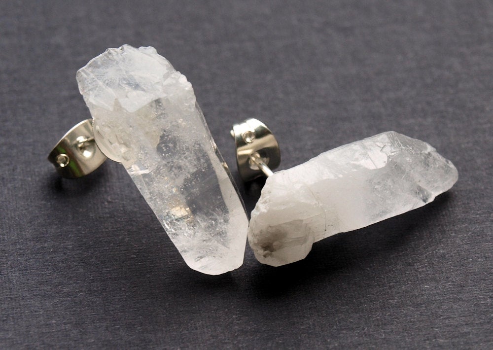 These Raw Quartz Point Earrings beautifully showcase two clear crystal studs with silver backings, artfully set against a dark surface. Ideal for those in pursuit of both style and spiritual development.