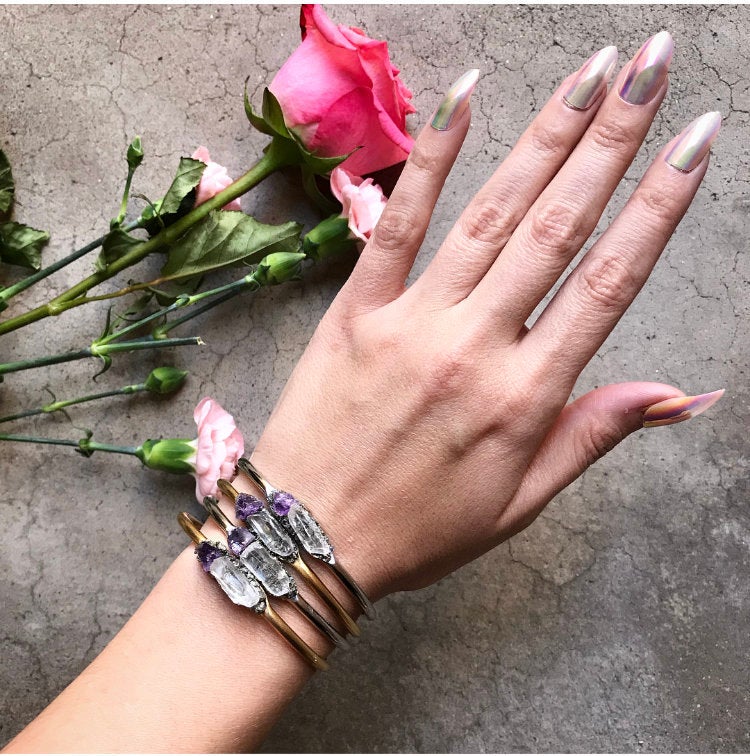 Introducing the Pyrite, Amethyst, and Quartz Bangle—a stunning silver cuff bracelet featuring an asymmetrical design with two raw crystals: a clear quartz famed for its healing properties and a beautiful purple amethyst set against a dark backdrop.