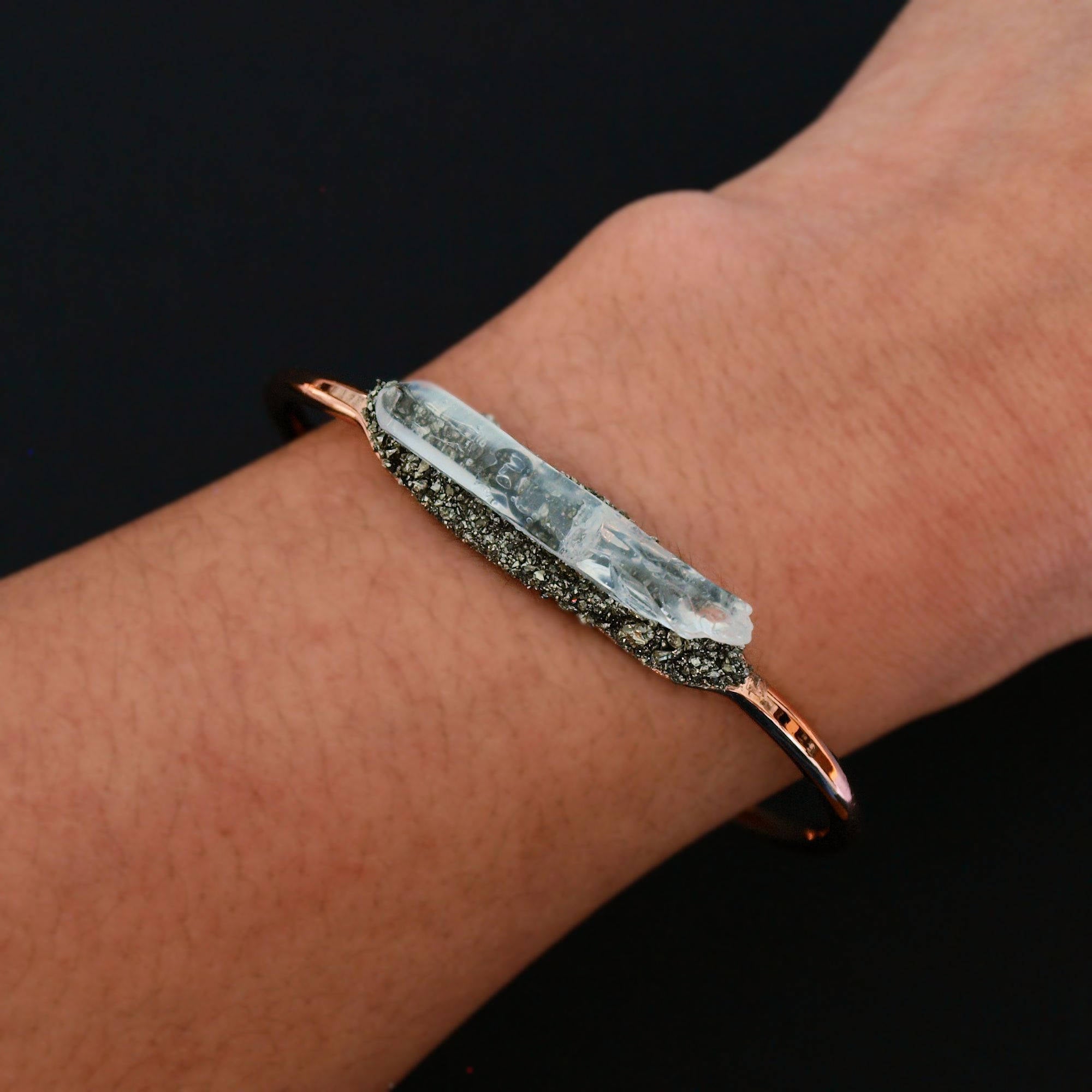The Rose Gold Pyrite and Quartz Bracelet features a prominent, clear crystal accented with metallic elements, elegantly displayed on a wrist against a dark backdrop.
