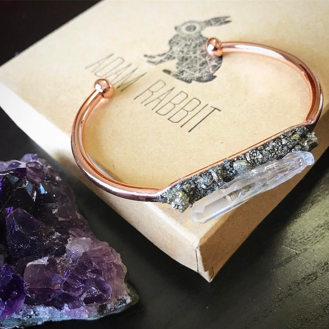 The Rose Gold Pyrite and Quartz Bracelet features a prominent, clear crystal accented with metallic elements, elegantly displayed on a wrist against a dark backdrop.