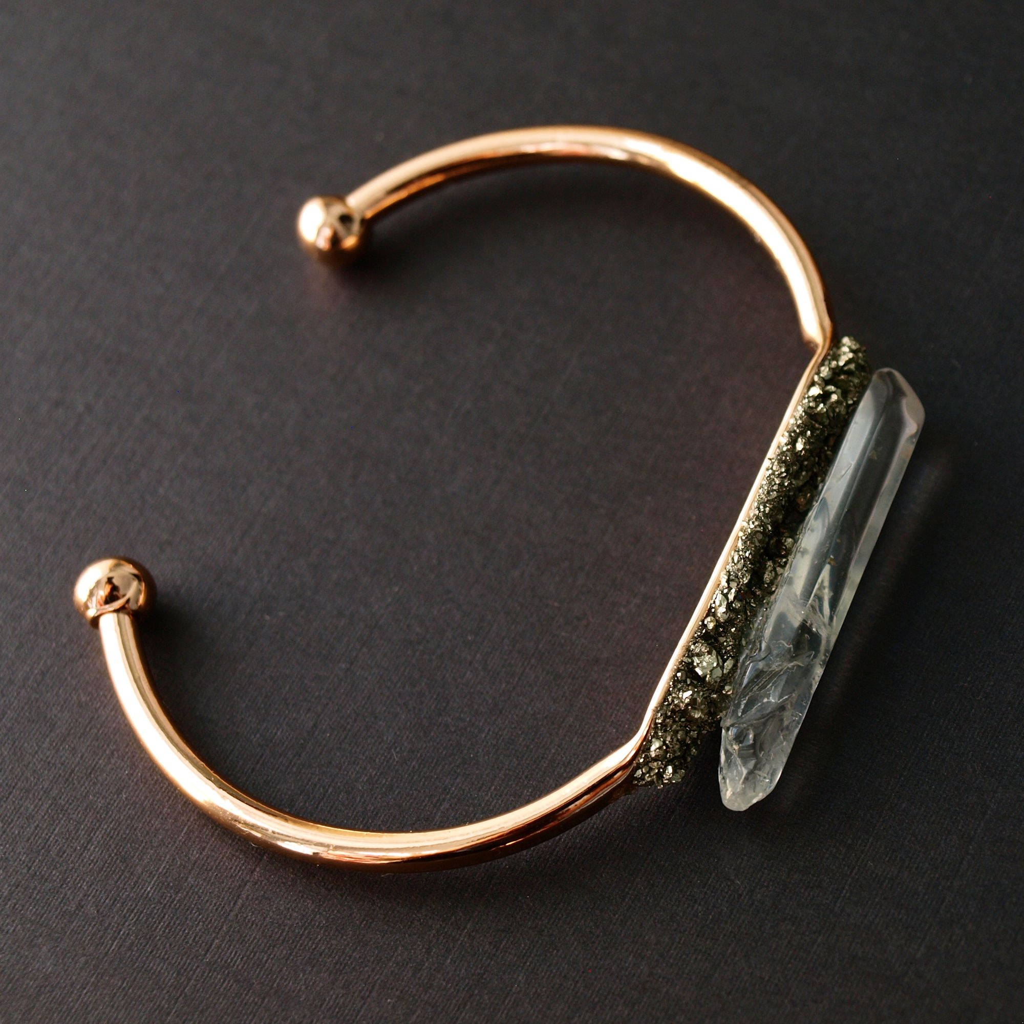 The Rose Gold Pyrite and Quartz Bracelet features a prominent, clear crystal accented with metallic elements, elegantly displayed on a wrist against a dark backdrop.