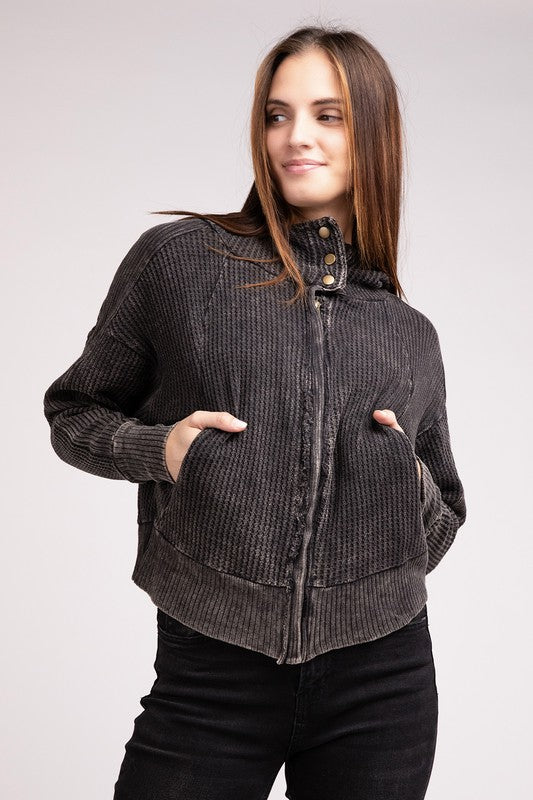 Woman in a Acid Wash Cotton Waffle Hooded Zip-Up Jacket with pockets and black pants, smiling and posing with hands on hips, against a light gray background.