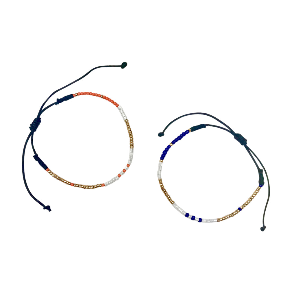 The Dori Beaded Bracelets, one showcasing orange, white, and gold beads and the other blue, white, and gold beads with adjustable cords, are elegantly displayed on a white background. These handmade jewels bring a sophisticated flair to any outfit.