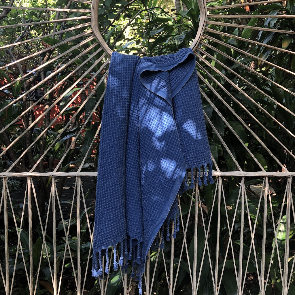 A folded, light gray blanket featuring a waffle texture and fringe tassels at the bottom mirrors the elegance of the Waffle Weave Turkish Towel, combining style and practicality for any cozy setting.