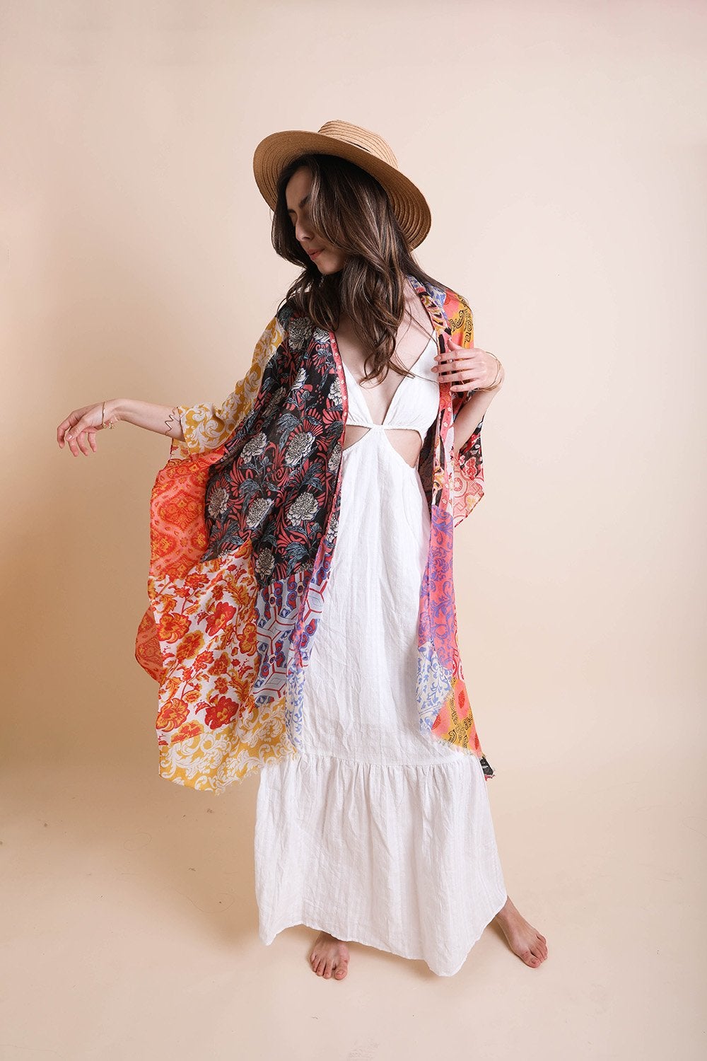 A person in a Boho Patchwork Kimono over their everyday outfit and a hat stands in an outdoor area with a wooden sink and mirror.