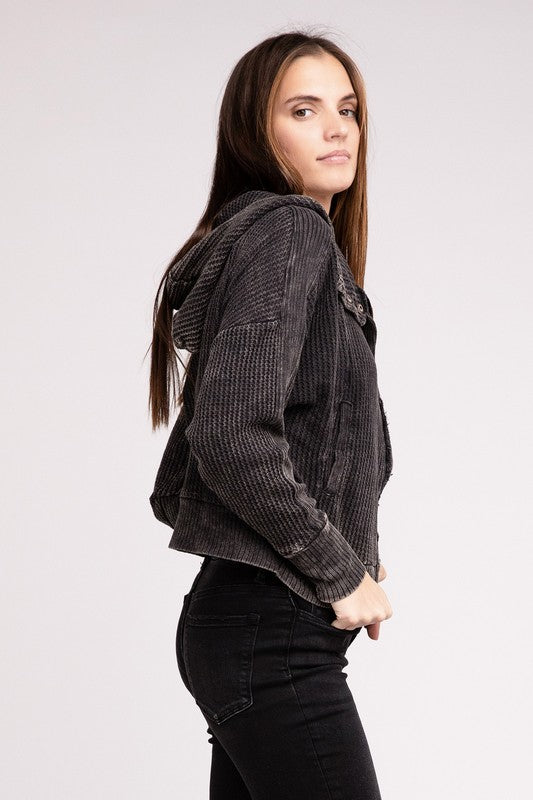 Woman in a Acid Wash Cotton Waffle Hooded Zip-Up Jacket with pockets and black pants, smiling and posing with hands on hips, against a light gray background.