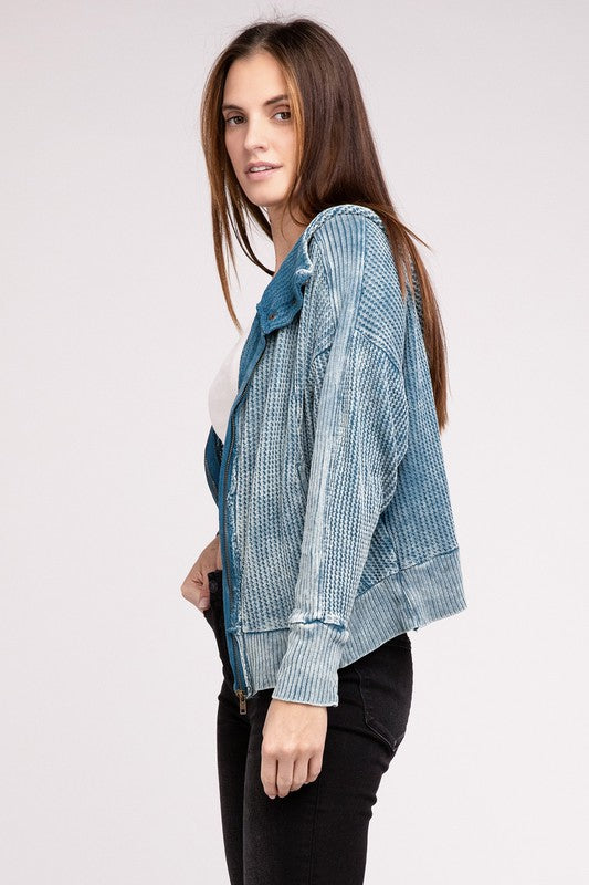 Woman in a Acid Wash Cotton Waffle Hooded Zip-Up Jacket with pockets and black pants, smiling and posing with hands on hips, against a light gray background.