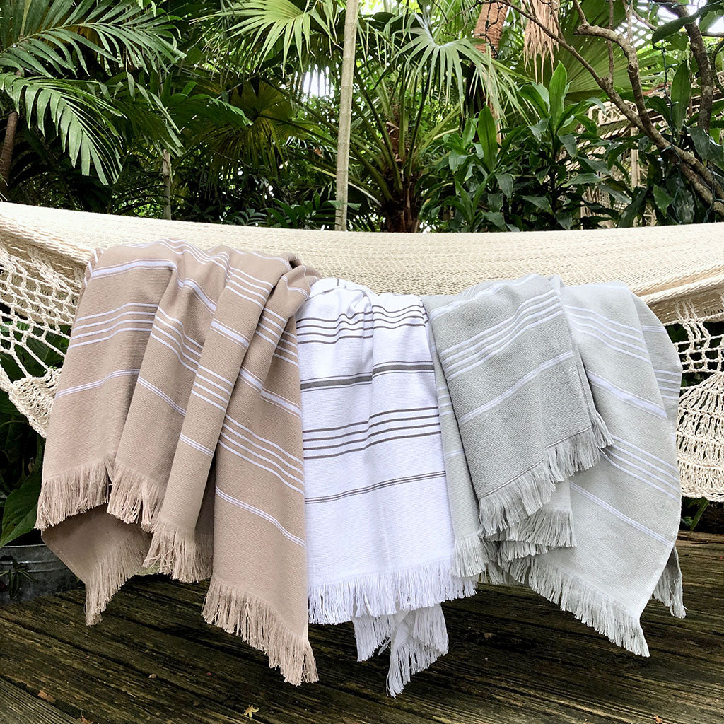 The Classic Terry Turkish Towel is a handmade white towel featuring horizontal gray stripes and fringed edges, ideal for enhancing the elegance of your bath collection.