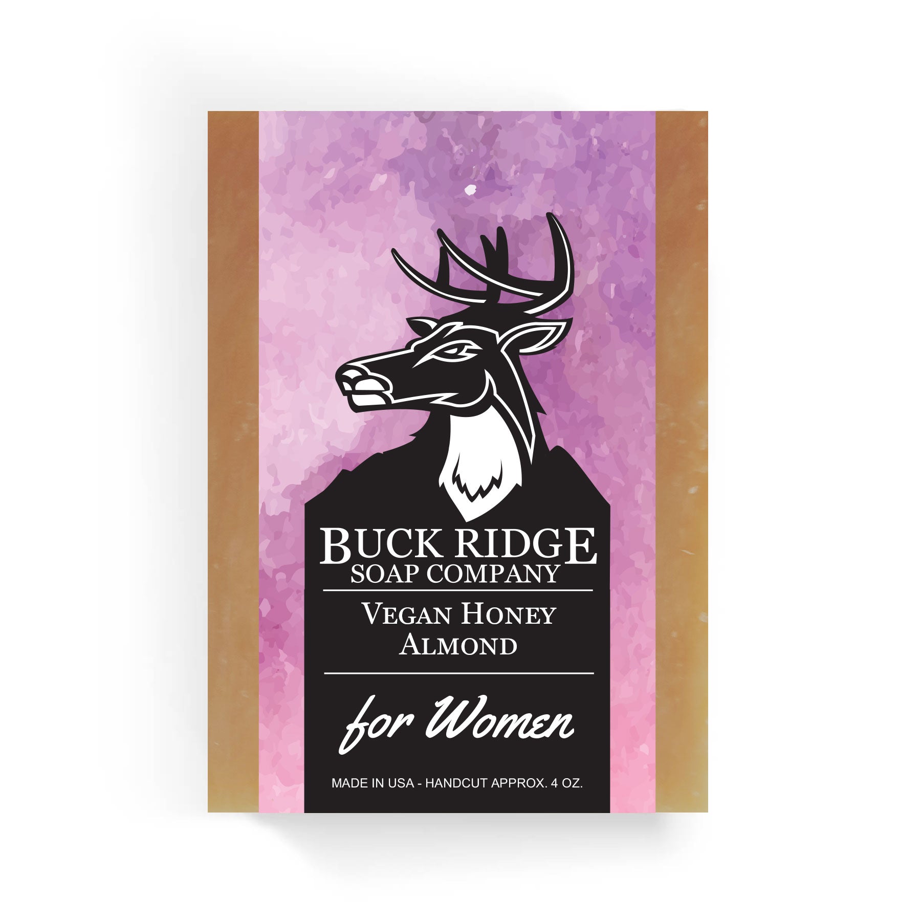 The packaging for the Vegan Honey Almond Handmade Soap by Buck Ridge Soap Company prominently features a deer logo alongside the text "Vegan Honey Almond for Women." Made in the USA, this handcrafted and handcut soap weighs approximately 4 oz. The packaging design stands out with a purple watercolor background, highlighting its natural ingredients.