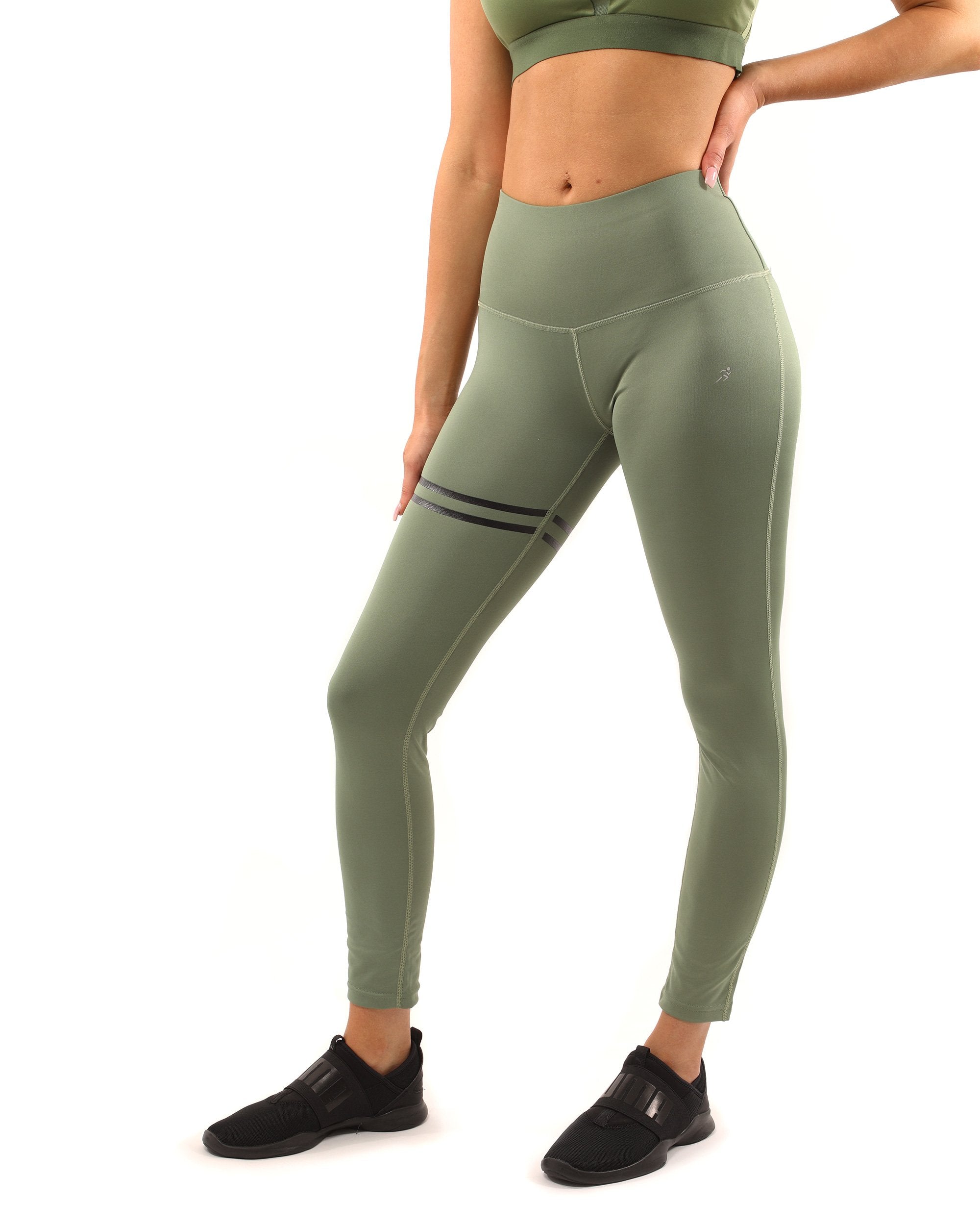 A person stands facing forward in the Huntington Set - Leggings & Sports Bra in Olive Green, paired with black shoes against a white background.