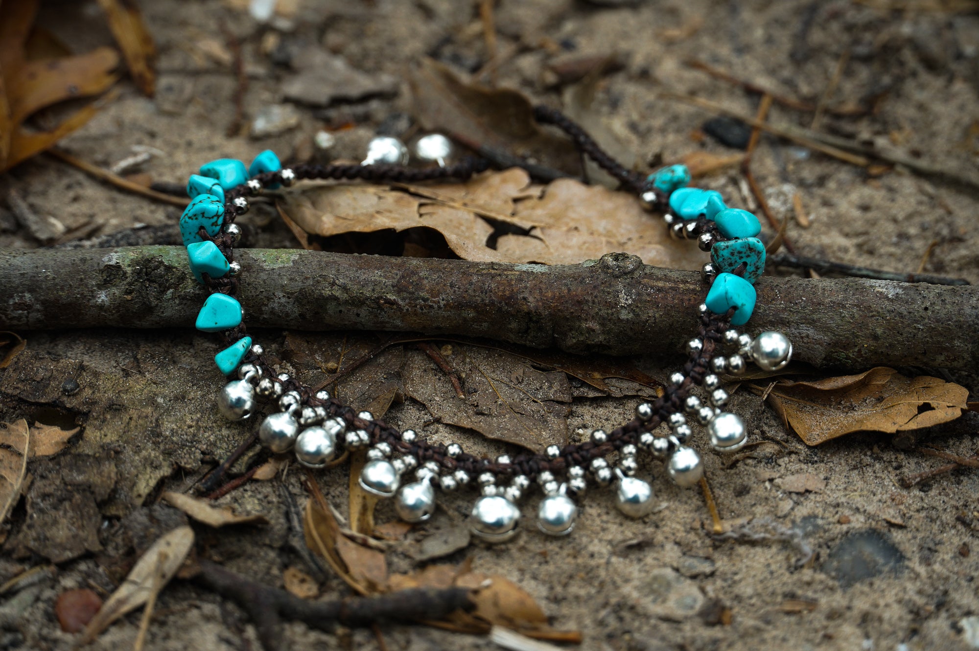 A woman's feet adorned with a Turquoise Silver Bell Boho Anklet are standing on rocks next to a body of water.