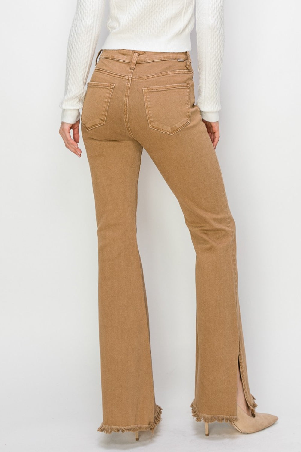 Wearing the RISEN Bailey Full Size High Waist Side Slit Flare Jeans with frayed hems, a person pairs them with beige boots against a white background.