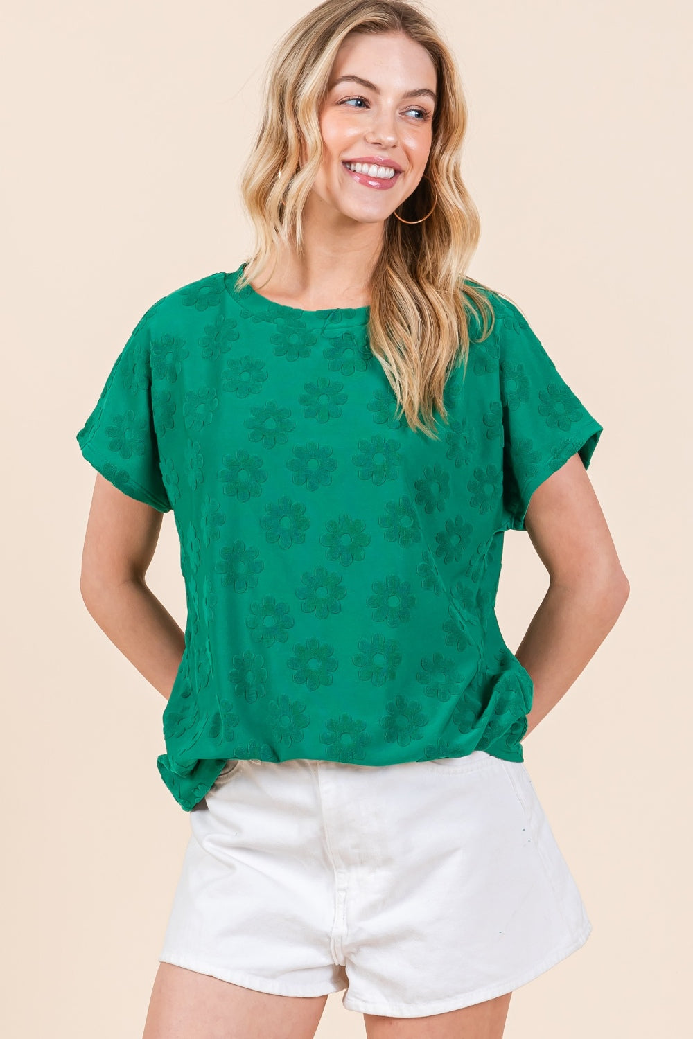 A person wearing the BOMBOM Textured Floral Pattern Short Sleeve T-Shirt in green paired with white shorts is smiling against a beige background.