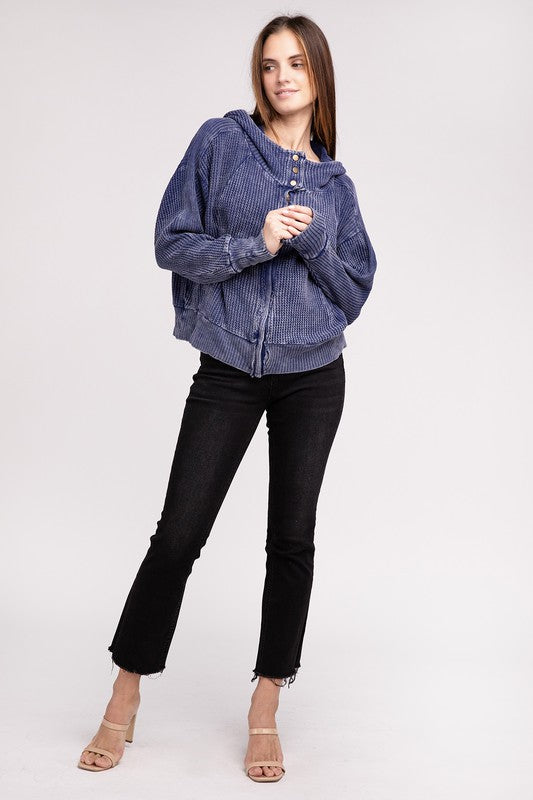 Woman in a Acid Wash Cotton Waffle Hooded Zip-Up Jacket with pockets and black pants, smiling and posing with hands on hips, against a light gray background.