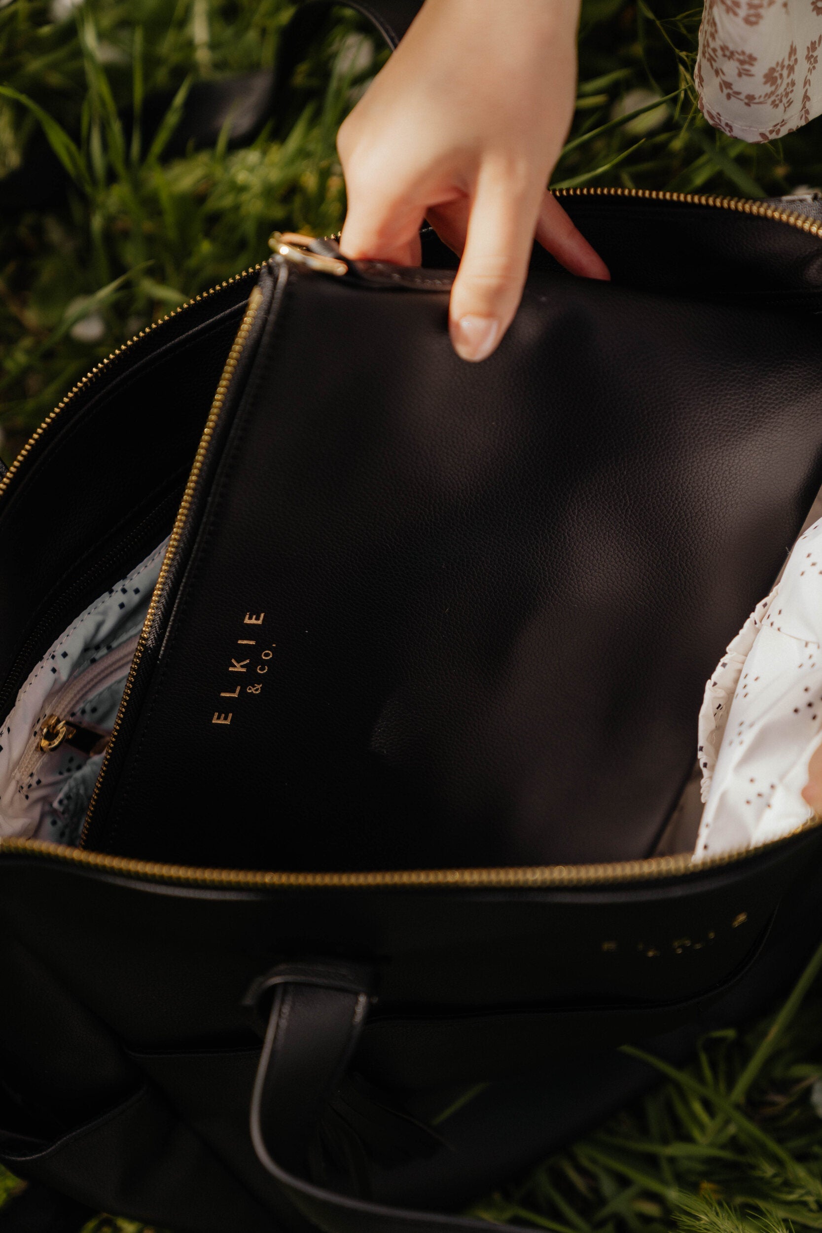 A person is standing against a white brick wall, showcasing The Aberdeen, a versatile brown leather backpack with multiple pockets.