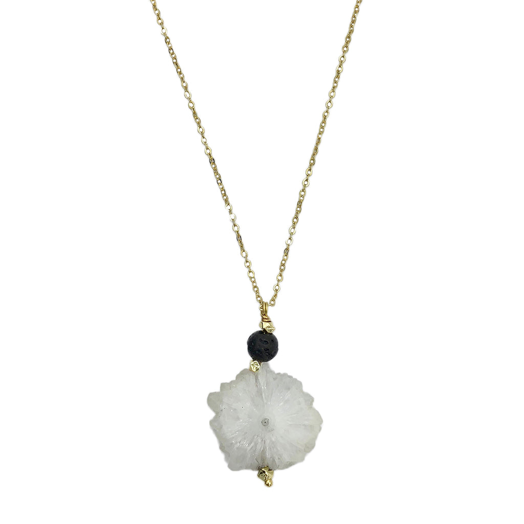 Introducing the Solar Quartz Lava Necklace: an artisan jewelry piece showcasing a gold chain adorned with a handmade white flower-shaped pendant and a small black bead.