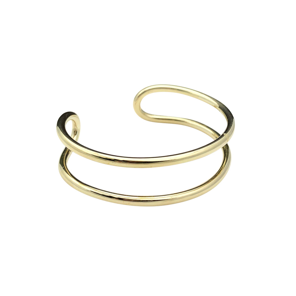 The Bombshell Wire Cuff is a gold double band cuff bracelet with an open-ended design, meticulously handmade in Cambodia. Crafted from recycled brass jewelry materials, this adjustable cuff combines both style and sustainability.