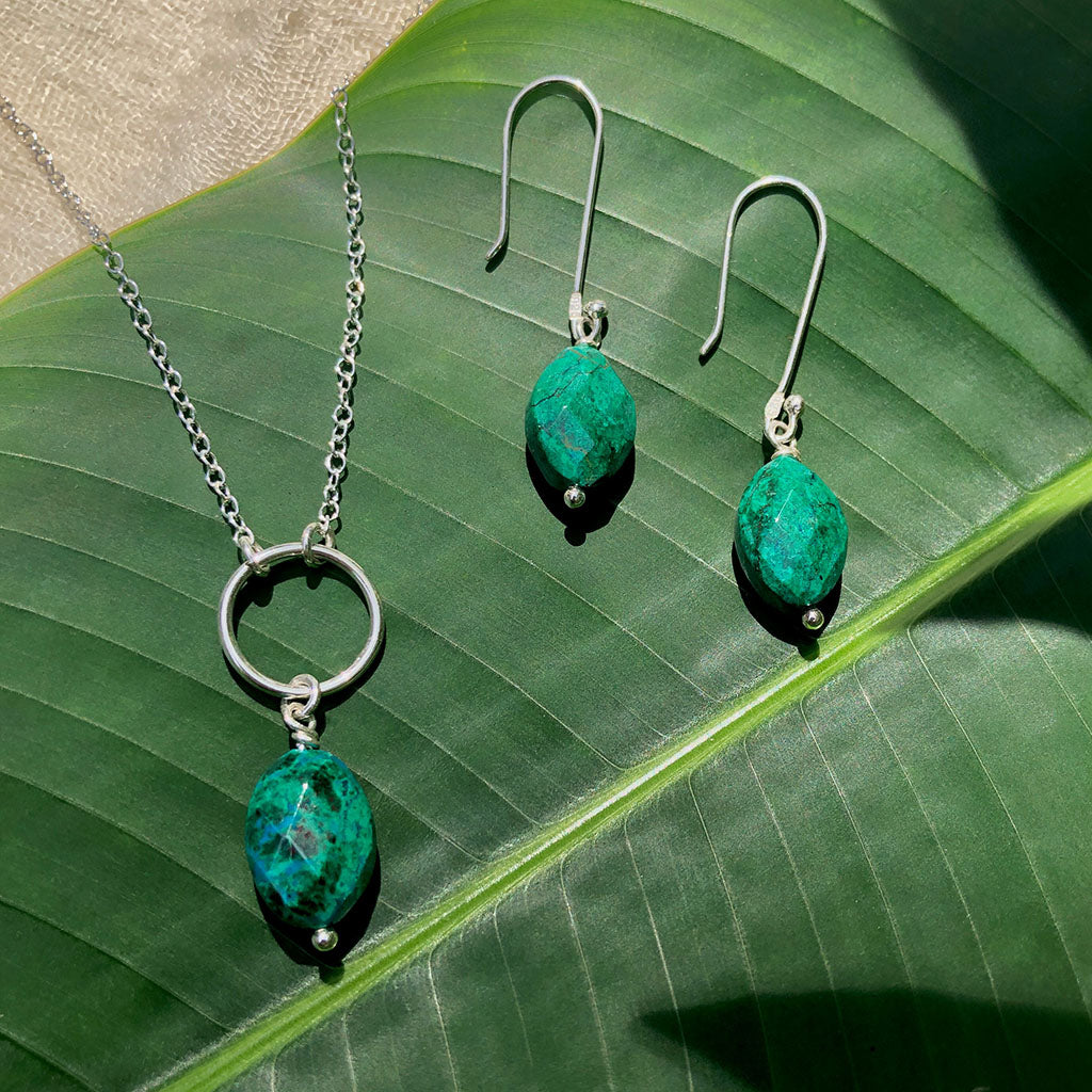 The Chrysocolla Circle Necklace is a handcrafted piece that includes a silver chain and a circular pendant, highlighting a dazzling Peruvian chrysocolla gemstone in rich green-blue tones.