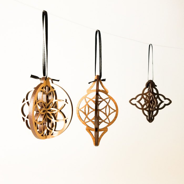 Three intricately carved Wood Christmas Ornaments hang from black ribbons against a white background, showcasing a modern ornament design.