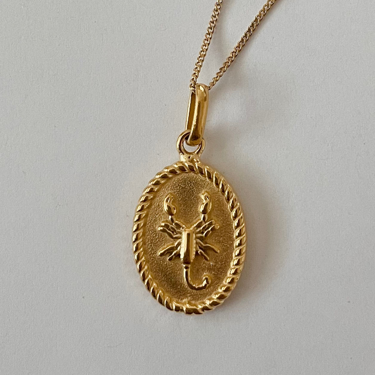 The Zodiac 2.0 Necklace - Gold features four gold-plated pendants with intricate designs, displayed vertically on a simple background, making it an ideal choice for an astrological necklace or hypoallergenic jewelry option.