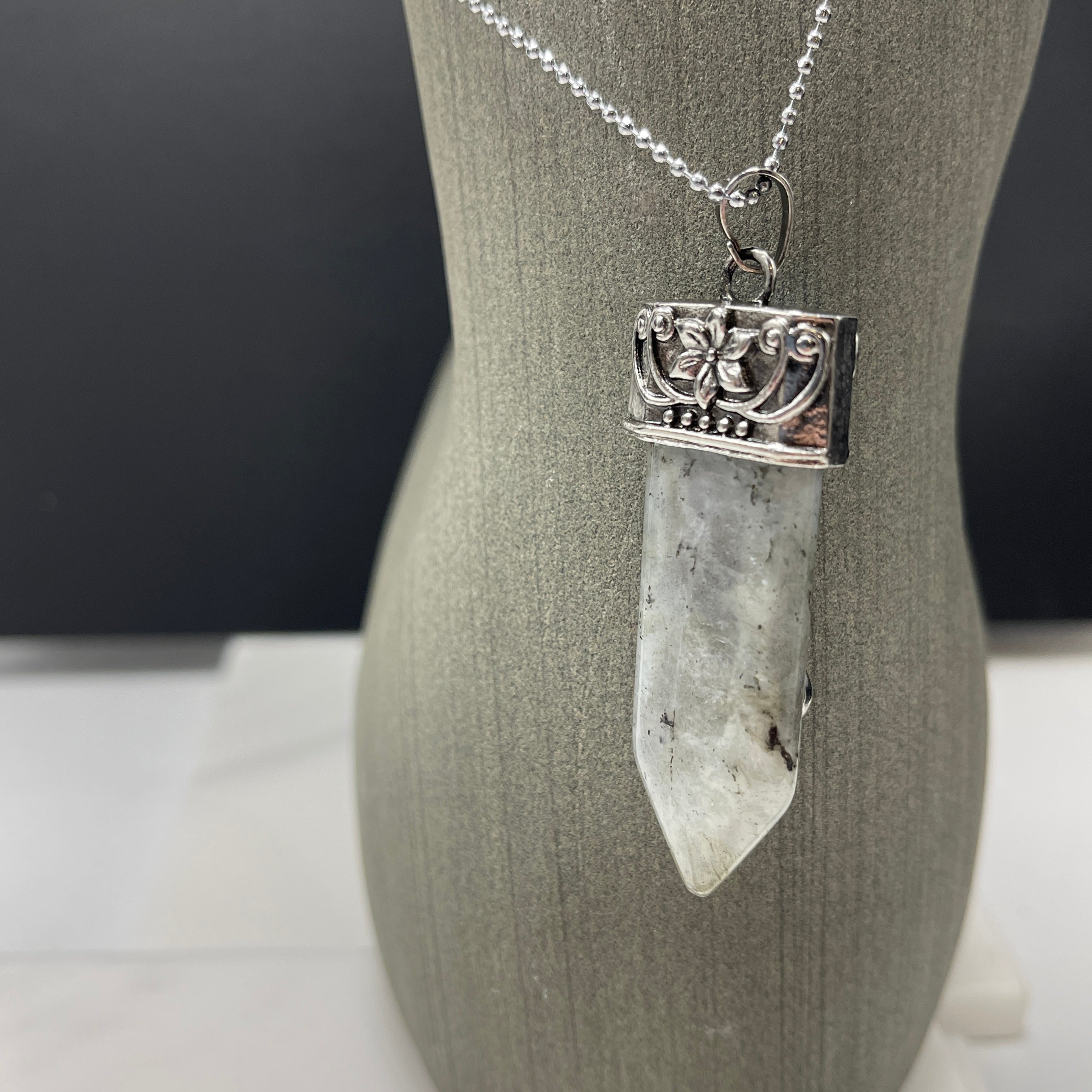 The Faerie Gemstone necklace features an enchanting opalite point adorned with intricate silver detailing, a small round moonstone, and a dangling amethyst. Accented with shimmering labradorite, it is elegantly showcased on a mannequin.