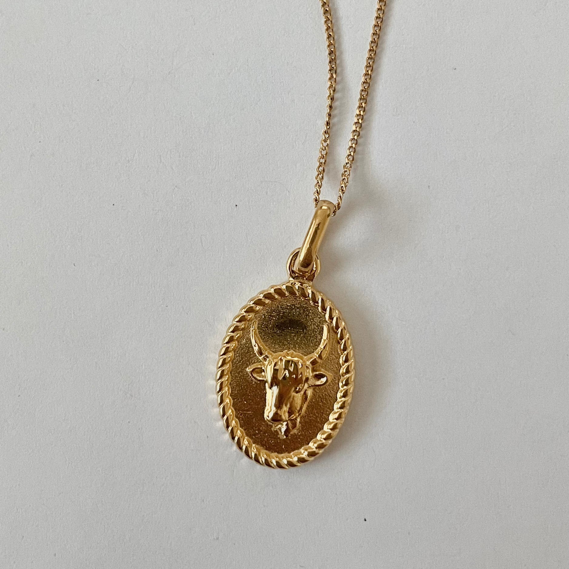 The Zodiac 2.0 Necklace - Gold features four gold-plated pendants with intricate designs, displayed vertically on a simple background, making it an ideal choice for an astrological necklace or hypoallergenic jewelry option.