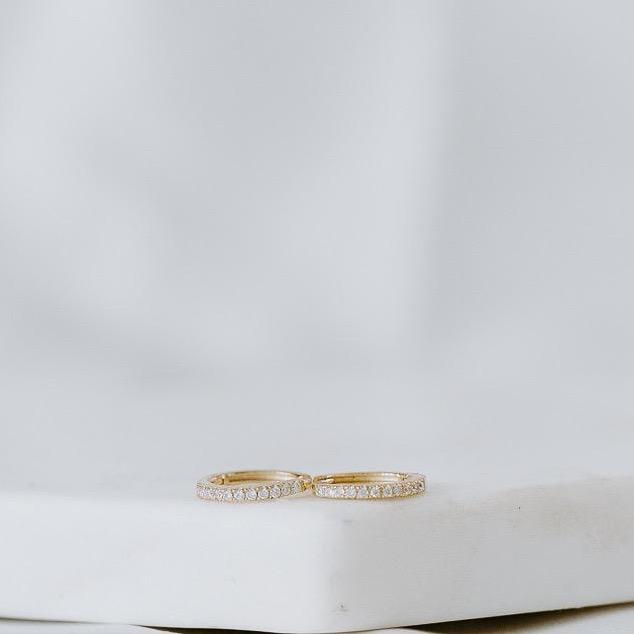 Four exquisite rings, named "Pave Huggies," crafted from 14k yellow and white gold and adorned with pave diamonds, are elegantly displayed on a white surface.