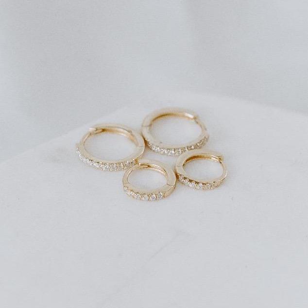 Four exquisite rings, named "Pave Huggies," crafted from 14k yellow and white gold and adorned with pave diamonds, are elegantly displayed on a white surface.