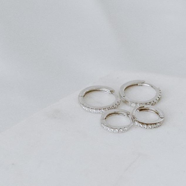 Four exquisite rings, named "Pave Huggies," crafted from 14k yellow and white gold and adorned with pave diamonds, are elegantly displayed on a white surface.