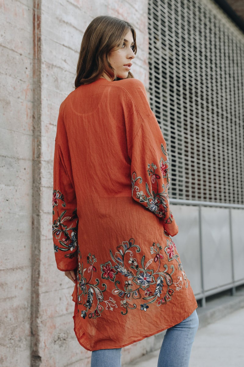 A woman in a Long Floral Kimono Cardigan stands by a brick wall, glancing over her shoulder.