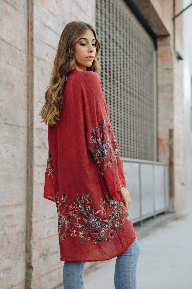 A woman in a Long Floral Kimono Cardigan stands by a brick wall, glancing over her shoulder.