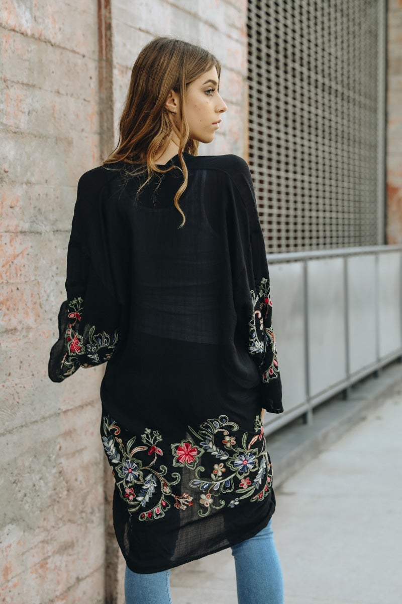 A woman in a Long Floral Kimono Cardigan stands by a brick wall, glancing over her shoulder.