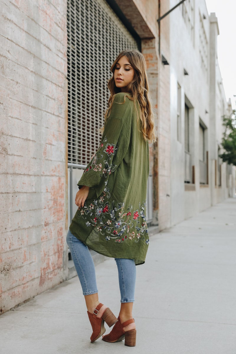 A woman in a Long Floral Kimono Cardigan stands by a brick wall, glancing over her shoulder.