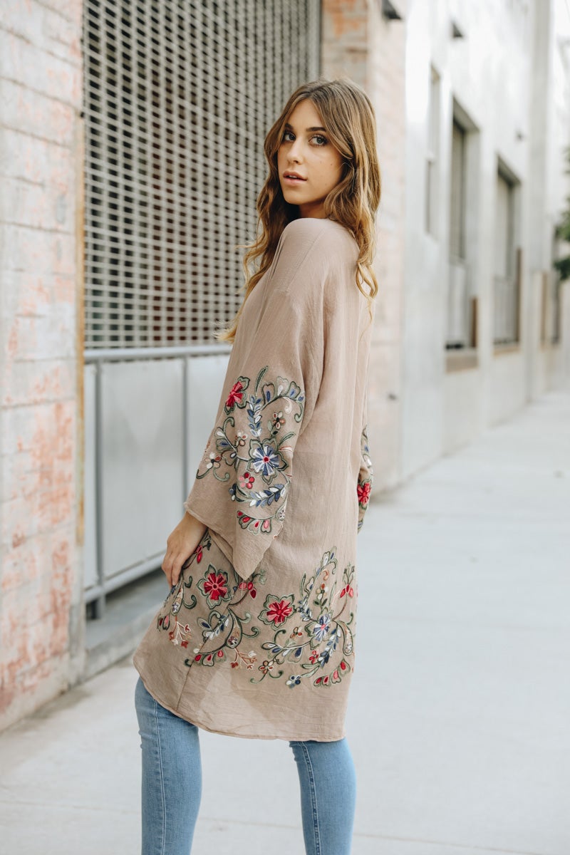 A woman in a Long Floral Kimono Cardigan stands by a brick wall, glancing over her shoulder.