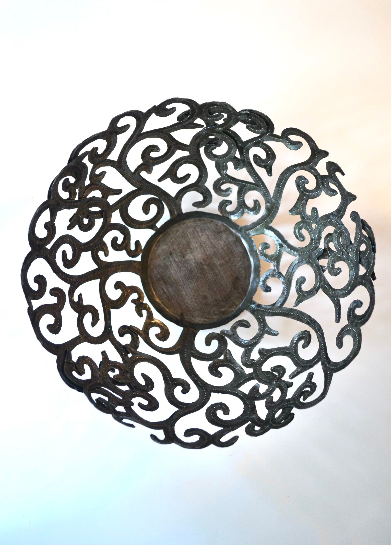 The Metal Art Scroll Bowl, intricately designed with swirling cut-out patterns and crafted from recycled steel, is elegantly displayed on a white surface.