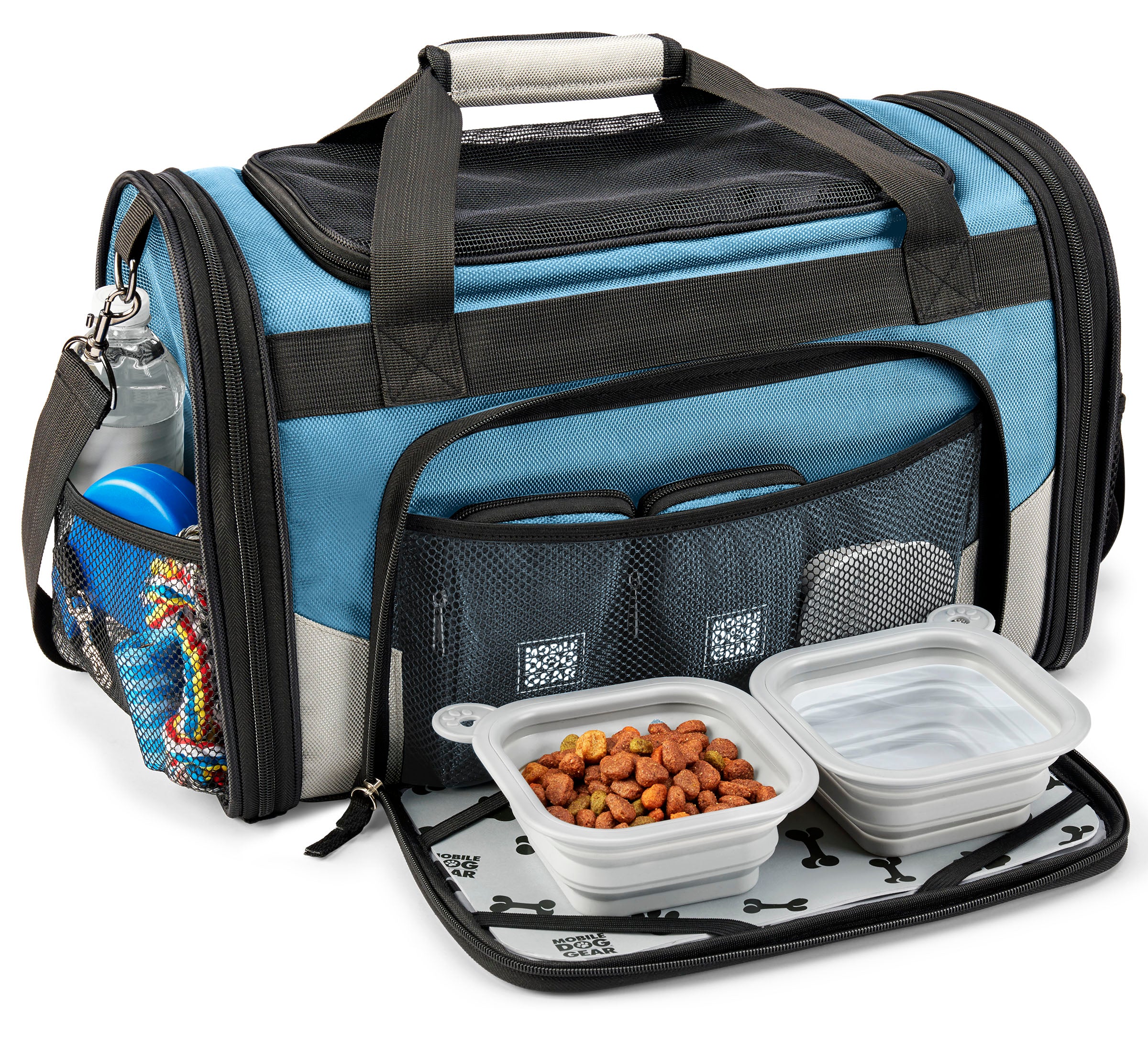 A small dog sits comfortably in a Mobile Dog Gear Pet Carrier Plus, complete with food and water bowls nearby. A speech bubble above says, "This is MY carrier!