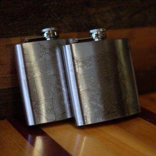 The Parker - Colorado Map Hip Flask lies on a wooden surface, accompanied by a small metal funnel and a white cloth drawstring bag.