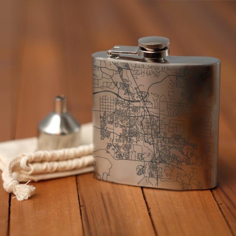The Parker - Colorado Map Hip Flask lies on a wooden surface, accompanied by a small metal funnel and a white cloth drawstring bag.