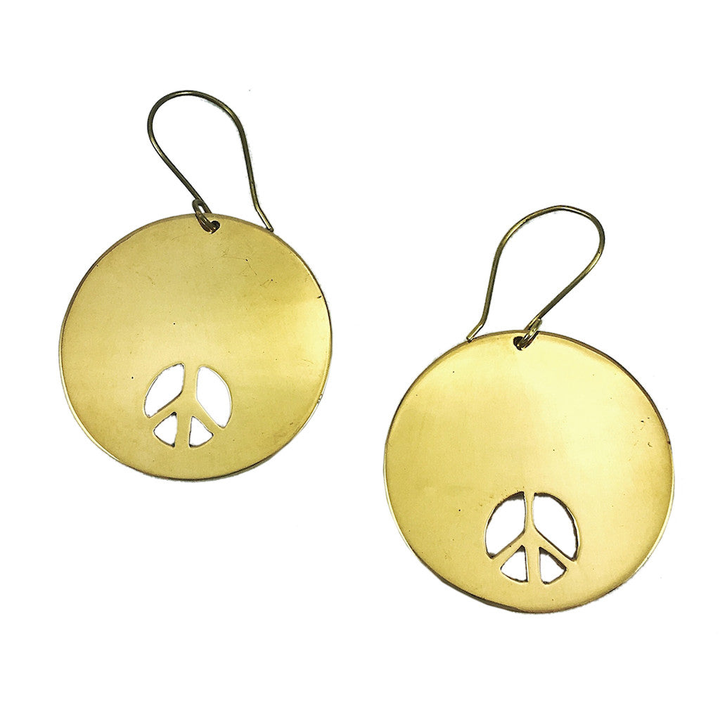 Crafted in Cambodia from recycled brass bombshells, the Bombshell Peace Earrings feature a gold-colored circular peace sign design with cutouts and hook attachments.