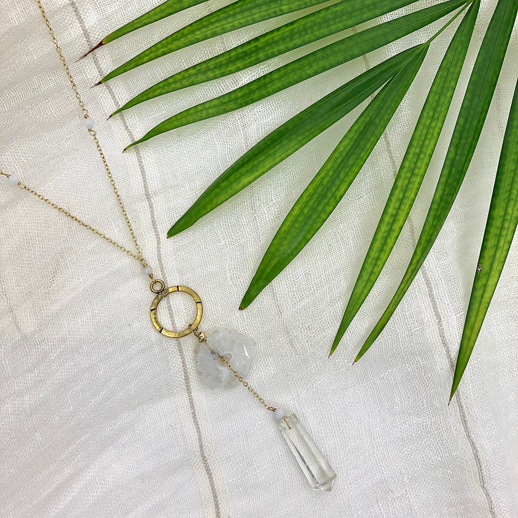 The Solar Quartz + Crystal Y Necklace is an enchanting piece of handmade jewelry, featuring a gold necklace with a circular pendant and two stunning stones, including solar quartz.