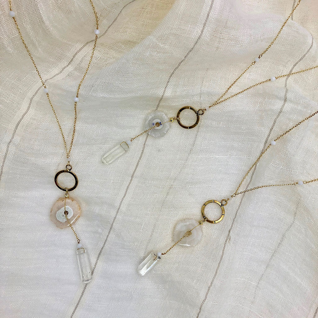 The Solar Quartz + Crystal Y Necklace is an enchanting piece of handmade jewelry, featuring a gold necklace with a circular pendant and two stunning stones, including solar quartz.