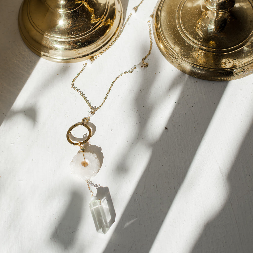The Solar Quartz + Crystal Y Necklace is an enchanting piece of handmade jewelry, featuring a gold necklace with a circular pendant and two stunning stones, including solar quartz.