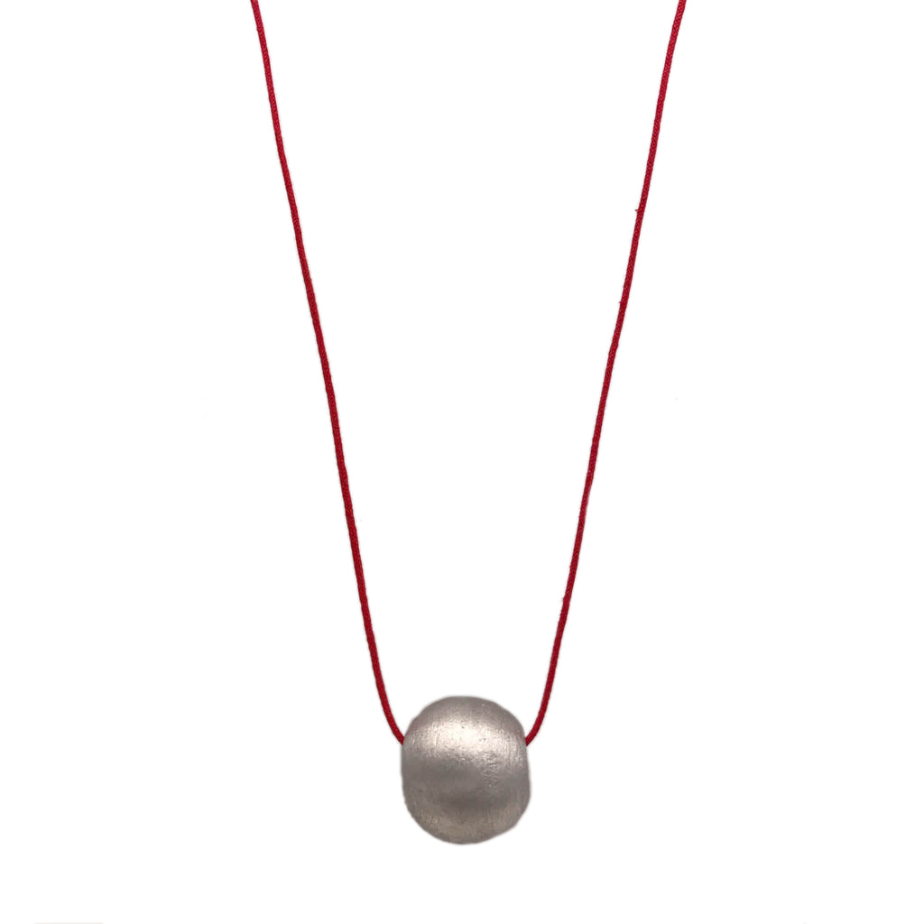 The Recycled Bombshell Ball Necklace is a stunning spherical pendant made from silver, hanging on a black cord. It is meticulously handcrafted by artisans in Laos using recycled bomb materials. Displayed against a white background, the necklace elegantly highlights the unique beauty of artisan jewelry.