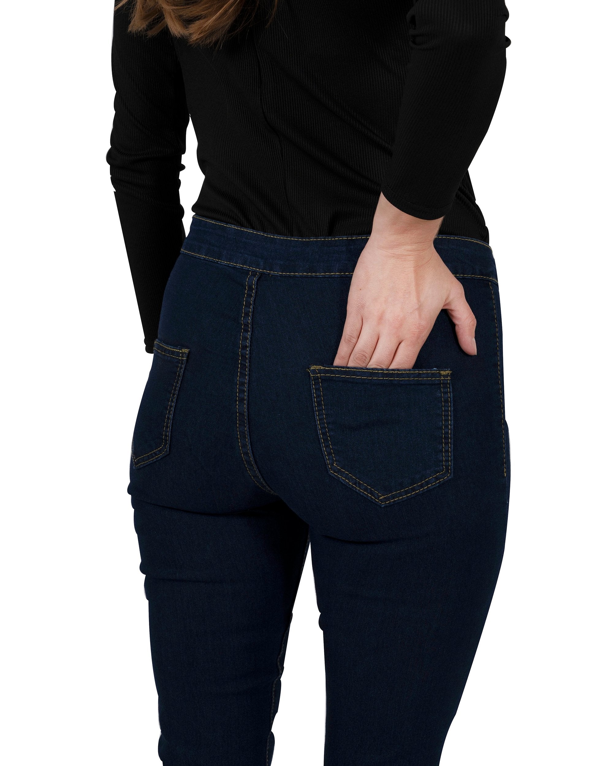 A woman in a black turtleneck and navy Walden Skinny Jeans stands with one hand on her hip, smiling.