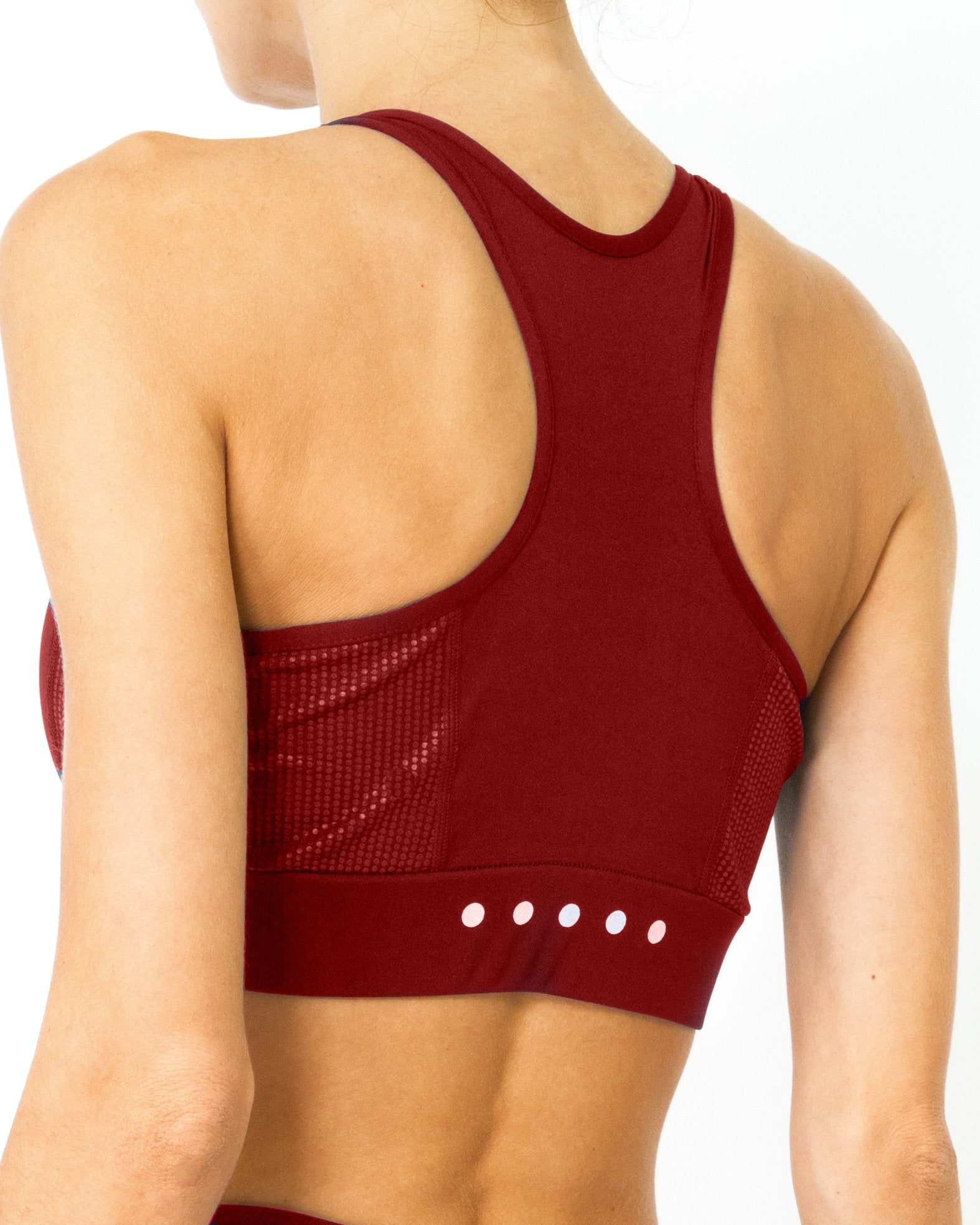 A person with hair in a bun is looking down while wearing the Ashton Sports Bra in maroon against a white background.